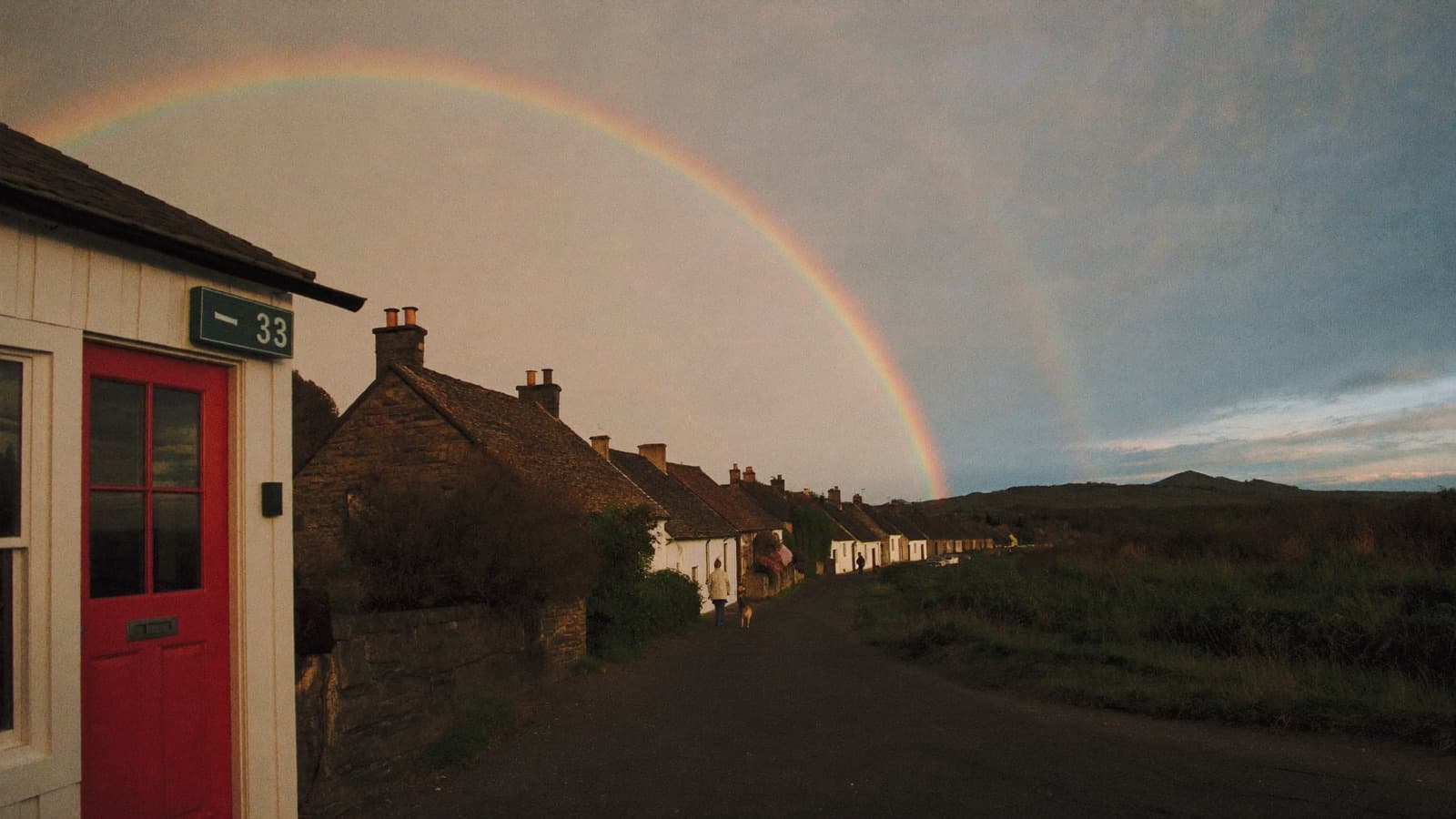 A double rainbow arcing over a small village street, a red front door in the foreground